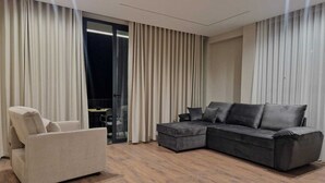 A modern living room with a grey sectional sofa, a beige armchair, and a glass door leading to a balcony. - Vila Kendezi (Vlorë)