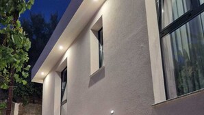 A modern building with stone steps leading to a door, a small window, and a light fixture on the wall. - Vila Kendezi (Vlorë)