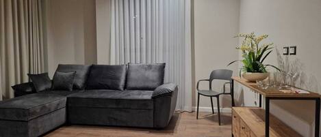 Una sala moderna con un sofá modular, una mesa de centro de madera y una mesita auxiliar con una planta.