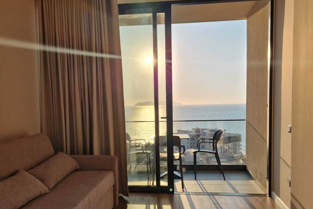 Una sala de estar moderna con un sofá, puerta de vidrio que da a un balcón con vista al mar.