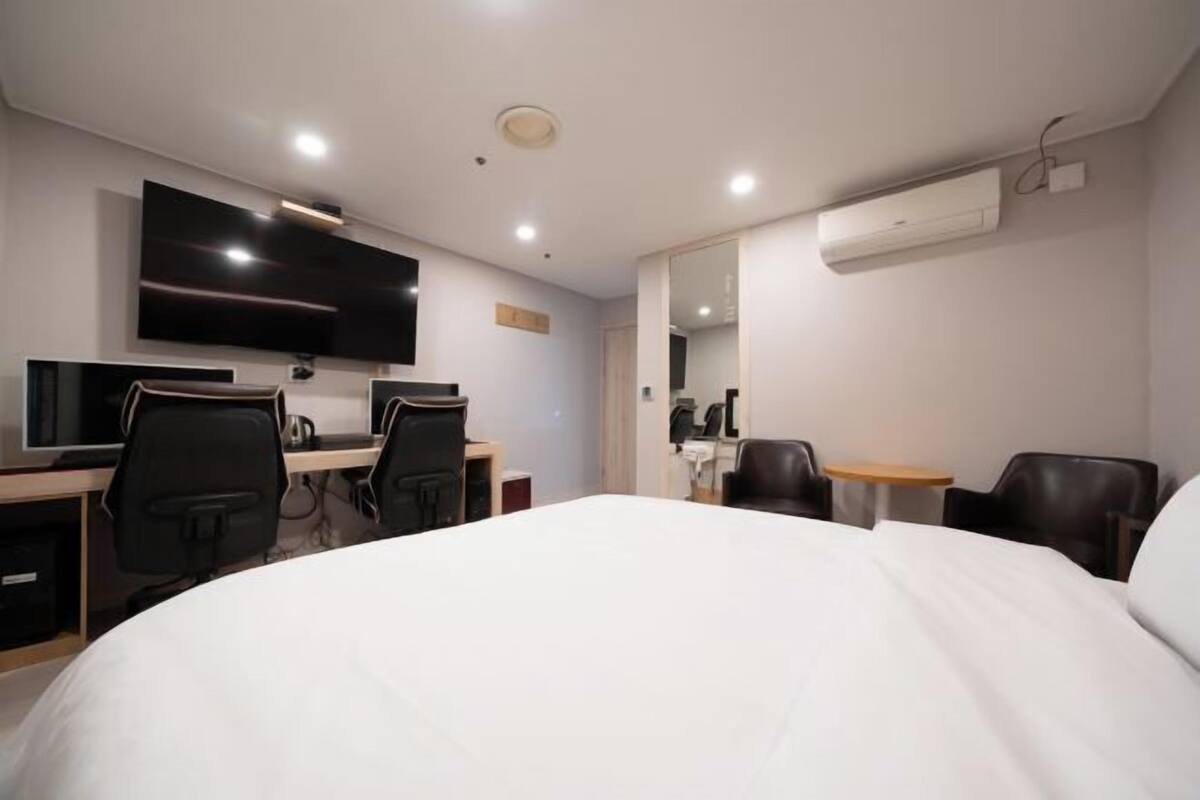 Una habitación de hotel con una cama grande, un escritorio con computadora, un televisor y una pequeña mesa con sillas.