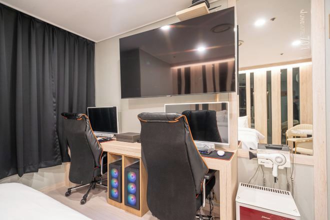 A modern hotel room with a large bed, a desk with two monitors, a hairdryer, and a mirror.