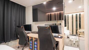 A modern hotel room with a large bed, a desk with two monitors, a hairdryer, and a mirror.