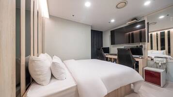 A modern hotel room with a bed, desk, chair, and a small desk with a computer and phone.