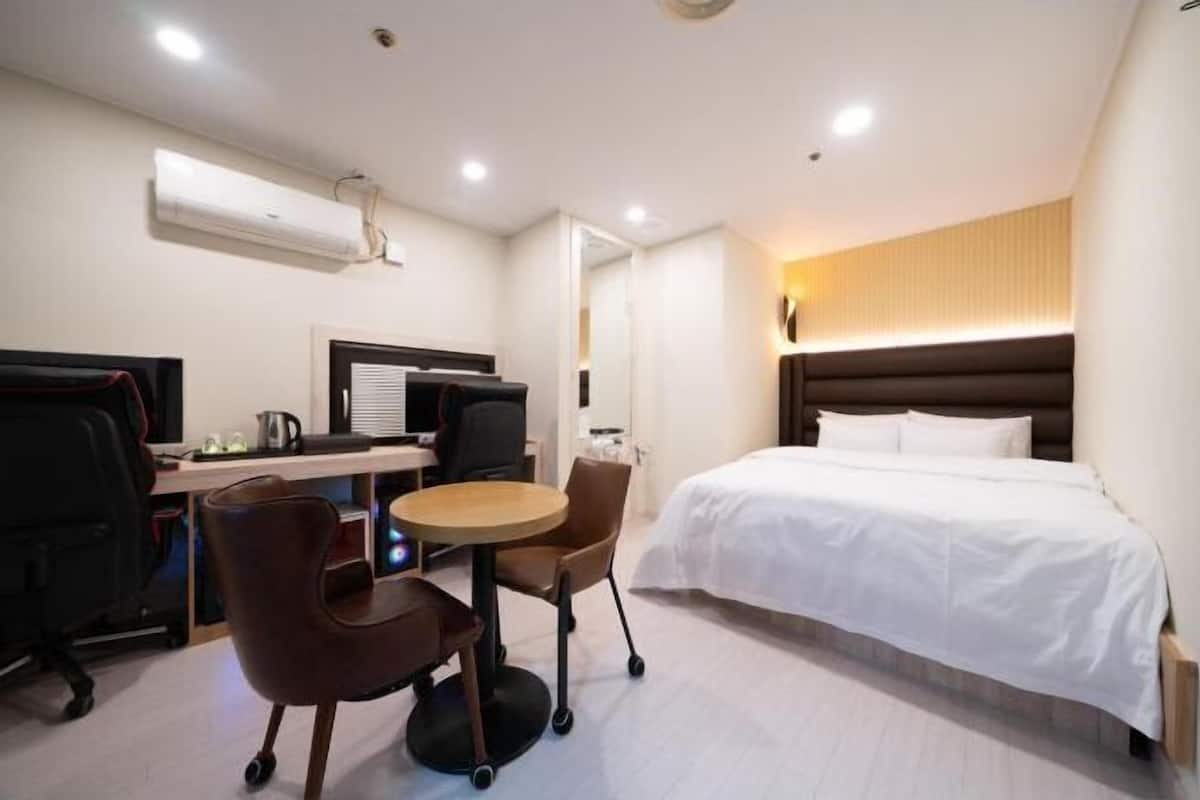 Una habitación de hotel con cama, escritorio, sillas y aire acondicionado.
