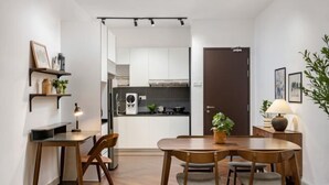 A compact kitchen with white cabinets, a stove, and a microwave. There is a dining area with a wooden table and chairs.