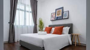 A modern hotel room with a large bed, grey curtains, a small plant, and framed artwork on the wall.