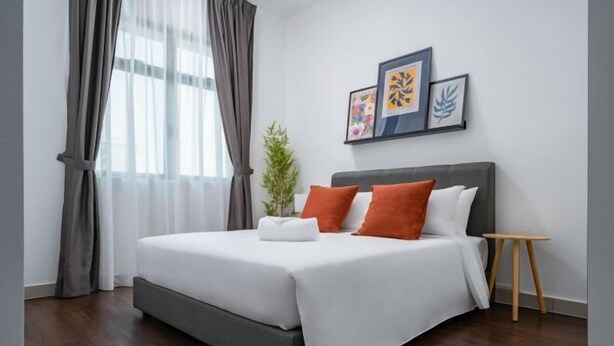 Une chambre d’hôtel moderne avec un grand lit, des rideaux gris, une petite plante et des œuvres d’art encadrées accrochées au mur.