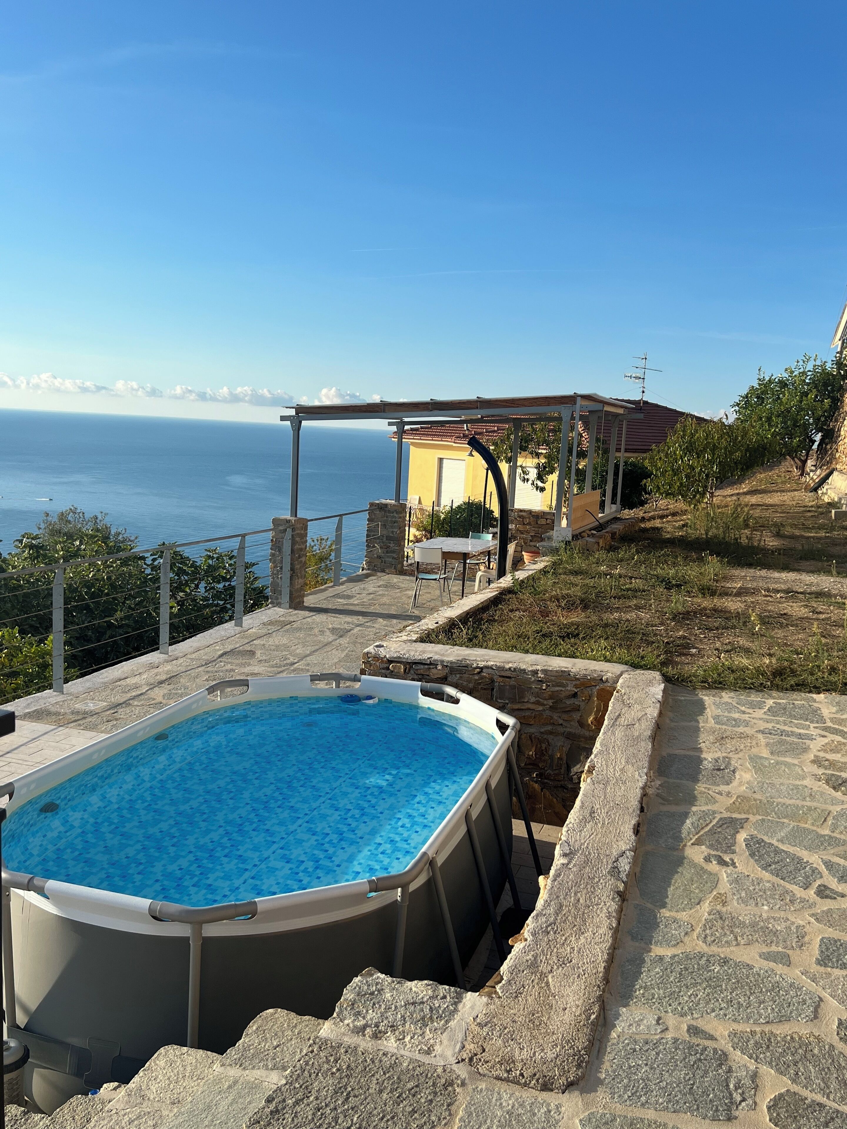 A swimming pool with a stone deck, a pergola, and a view of the sea.