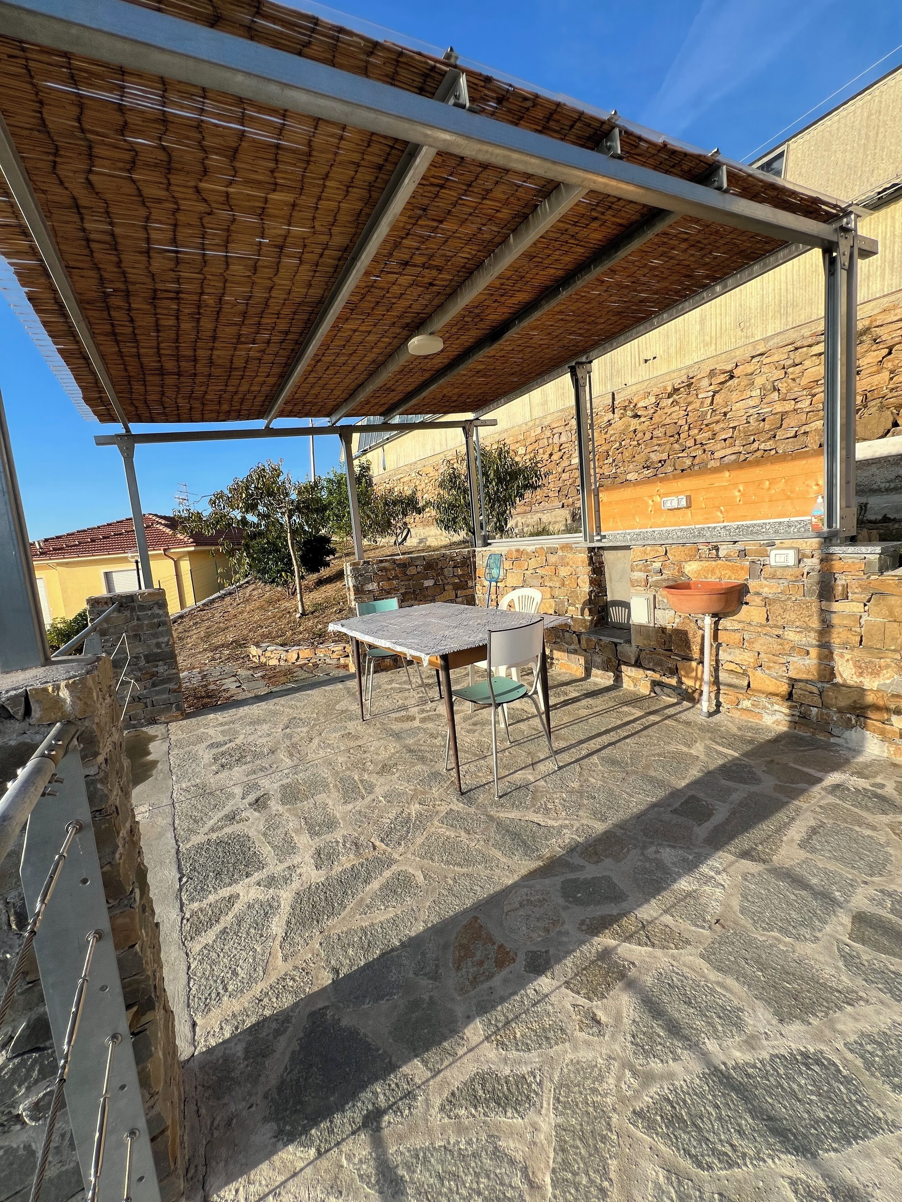 An outdoor patio with stone flooring, a table with chairs, a pergola, and a stone wall.