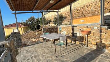 An outdoor patio with stone flooring, a table with chairs, a pergola, and a stone wall.