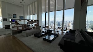 A spacious living room with a large window offering a city view, a modern sofa, a coffee table, and a bookshelf. - Ritz Residence Platinum KL (Kuala Lumpur)