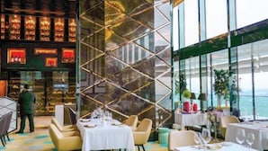 A restaurant with a modern interior, featuring a geometric wall design, white tablecloths, and a view of the sea. - Ritz Residence Platinum KL (Kuala Lumpur)