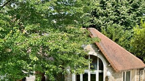 Een stenen cottage met een pannendak, grote ramen en een weelderige tuin.