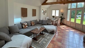 Een ruime woonkamer met een hoge plafond, zichtbare houten balken, een groot raam en een eethoek.