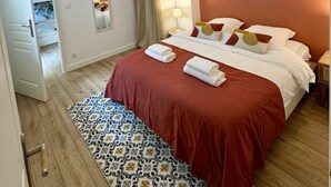 Een hotelkamer met een groot bed, een kamerkleed met dessin, een kroonluchter en uitzicht op een balkon.