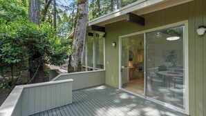 Une terrasse extérieure moderne avec un plancher en bois, une porte vitrée donnant sur un espace intérieur et une vue sur un coin repas à travers la vitre.