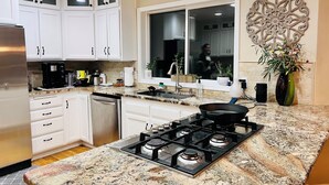 Une cuisine avec des meubles blancs, un réfrigérateur en acier inoxydable, une cuisinière à gaz et une fenêtre agrémentée d’un élément décoratif mural.