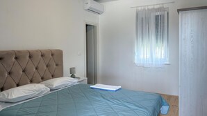 A bedroom with a tufted headboard, a bed with a blue quilt, a bedside lamp, and a window with sheer curtains. - Gorgeous apartment in Sukosan with WiFi (Sukosan)