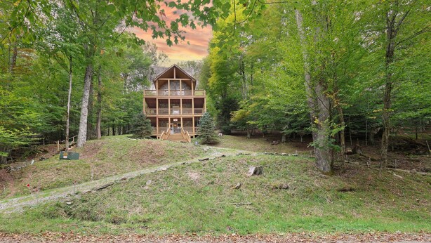 A two-story log cabin with a balcony, surrounded by dense forest.