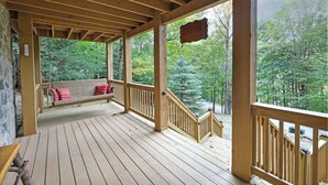 A wooden deck with a bench and a hanging sign, overlooking a forested area.