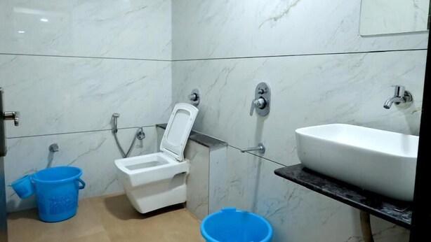 A bathroom with a toilet, sink, and shower. There are two blue buckets on the floor. - Hotel Season (Ahmedabad)