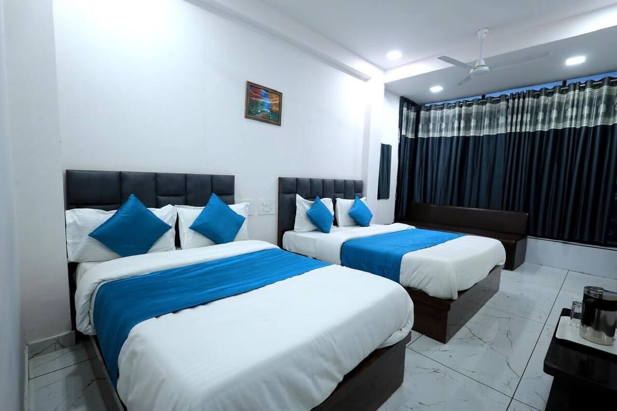A hotel room with two beds, each with white bedding and blue accents, a ceiling fan, and a window with dark curtains.