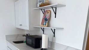 Uma cozinha compacta com armários brancos, micro-ondas, pia e um rolo de papel toalha no balcão.
