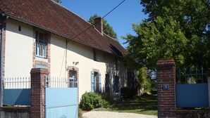A two-story house with a brick facade, a blue gate, and a gravel driveway.