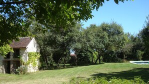 A stone house with a sloped roof, surrounded by a well-maintained lawn and dense trees.