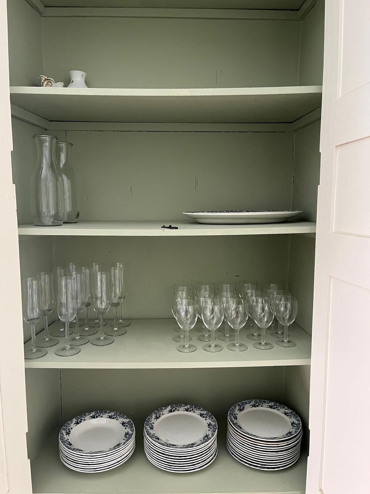 A white cabinet with shelves containing clear glassware, plates, and vases.