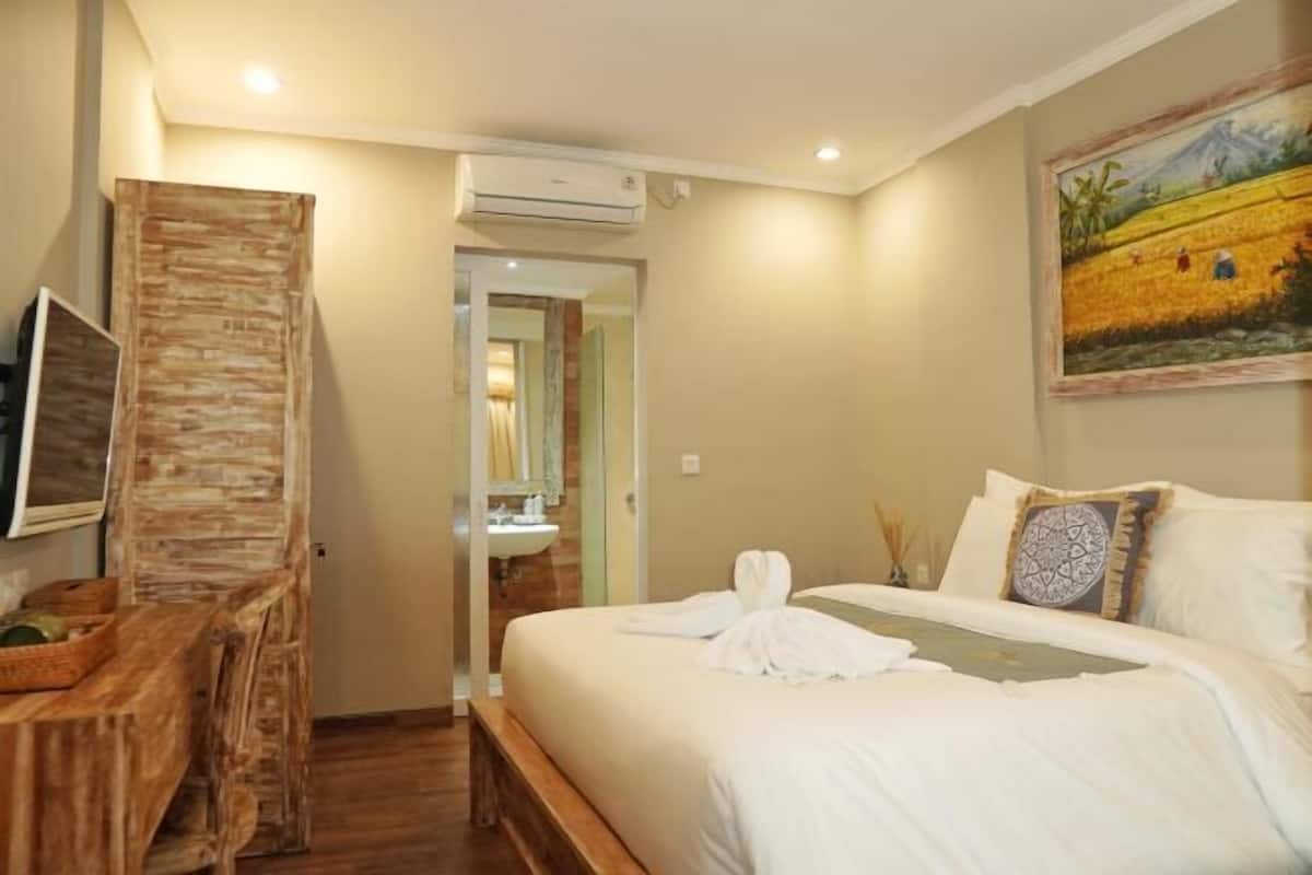 A hotel room with a bed, a desk, a television, and a painting on the wall.