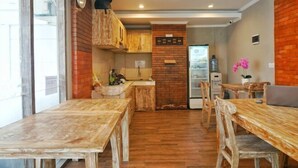 A rustic kitchen with wooden cabinets, a brick wall, and a dining area with a wooden table and chairs. - Koura Jimbaran (Bali)