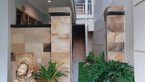 A hallway with stone pillars, a staircase, and green plants. - Koura Jimbaran (Bali)