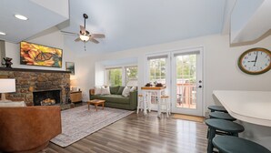 Ein geräumiges Wohnzimmer mit Kamin aus Stein, einem grünen Sofa, einem Holztisch und einem Essbereich mit weißen Hocker.