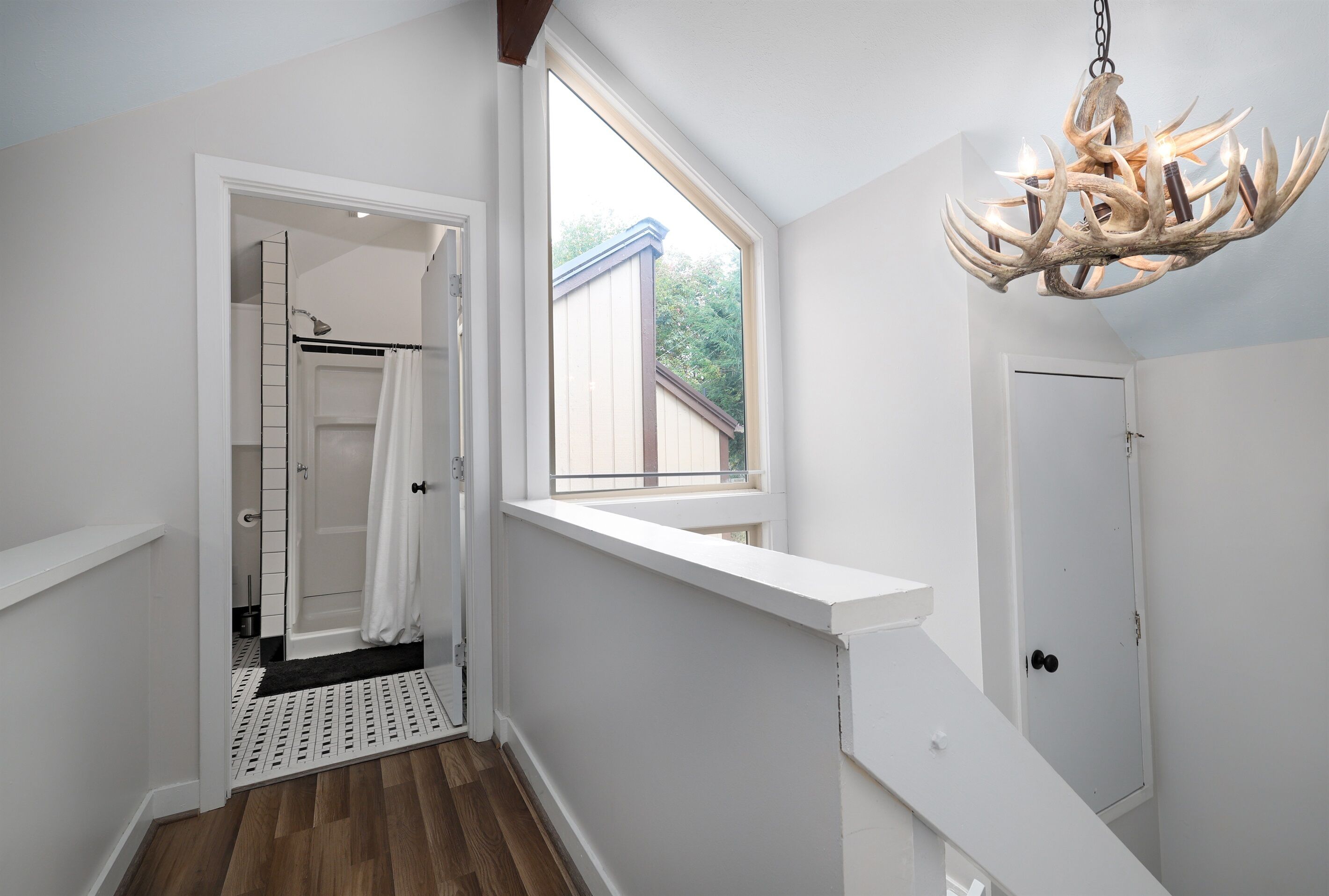 A modern bathroom with a shower, a window, and a chandelier.