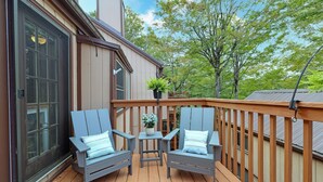 Eine Holzterrasse mit zwei grauen Adirondack-Stühlen und einem kleinen Tisch mit einem Blumentopf.