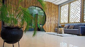 Un salon moderne agrémenté d’une grande plante en pot, d’un canapé bleu et d’un mur décoratif orné d’un motif géométrique.