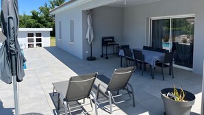 Un patio couvert avec des meubles d’extérieur, un barbecue et une plante en pot.