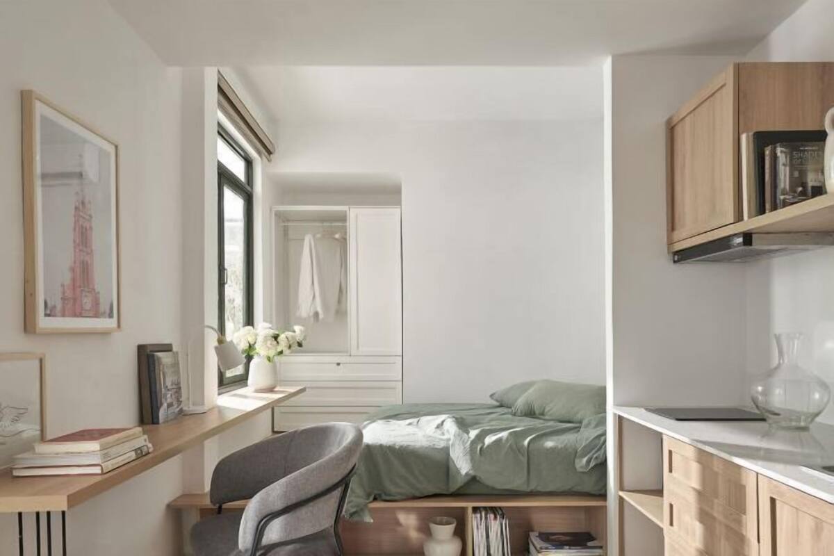 A bedroom with a bed, a desk with books, a chair, and a window.