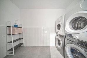 A laundry room with stacked washing machines, a shelf with laundry baskets, and a ladder. - Express by M Village Tran Quoc Thao, a brand of Modern Village Lifestyle (Ho Chi Minh City)