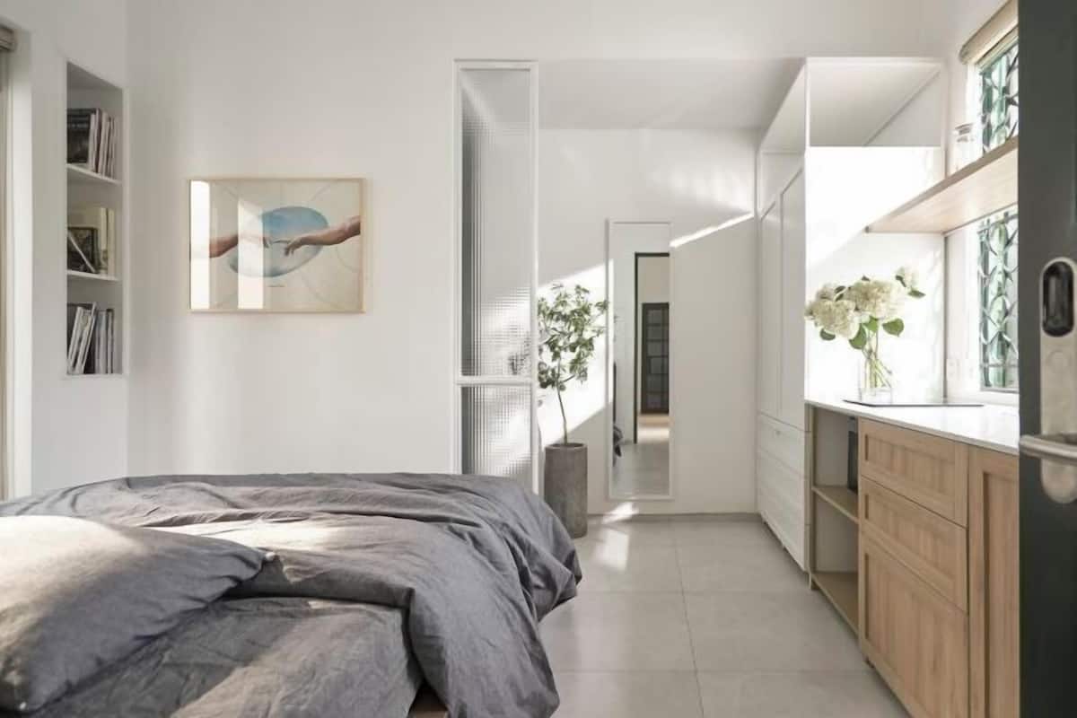 A modern bedroom with a large bed, a bedside bookshelf, and a painting on the wall.