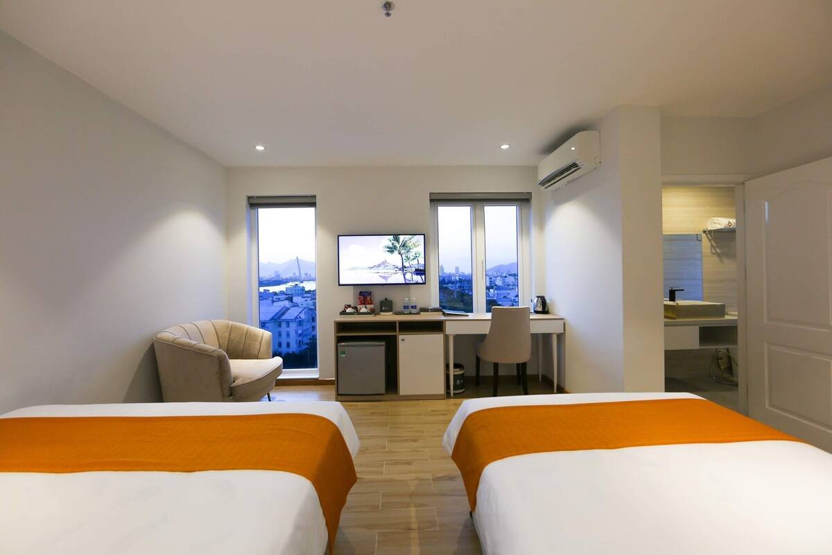 A hotel room with two beds, a desk with a computer, a TV, and a view of a cityscape.