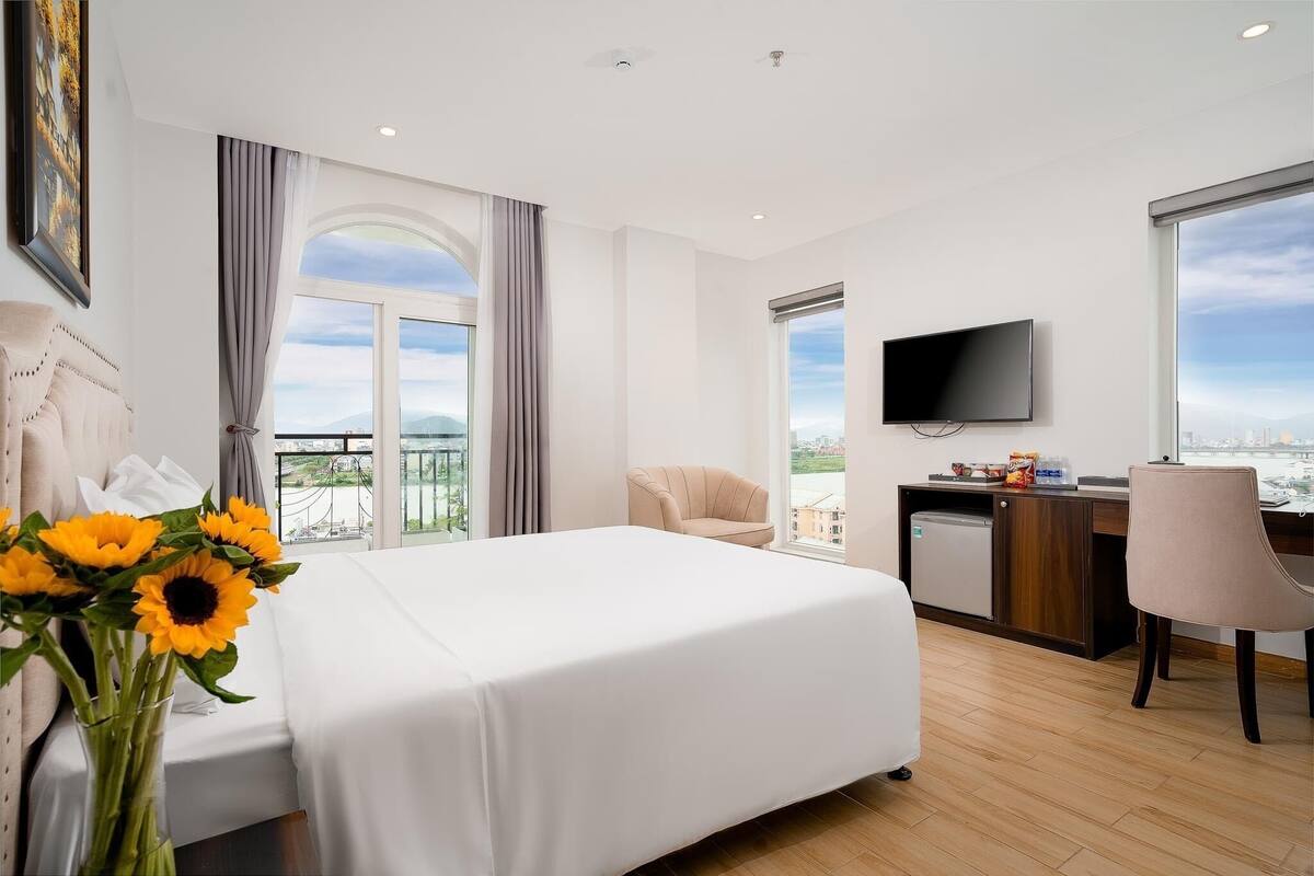 A hotel room with a bed, a desk, a TV, and a view of the city.