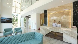 A modern hotel lobby with a reception desk, two receptionists, a large seating area, and a high ceiling with glass railings. - RHM Luxury Hotel and Suite  (Da Nang)