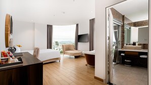 A hotel room with a bed, a desk, a chair, a bathtub, and a bathroom with a sink and mirror. - RHM Luxury Hotel and Suite  (Da Nang)