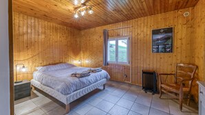 Une chambre à coucher aux murs lambrissés, avec un lit, des lampes de chevet, un radiateur et une fenêtre.