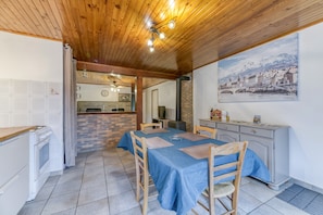 Un coin repas avec une table dressée pour quatre personnes, une cuisine équipée d’une cuisinière et un tableau représentant une ville enneigée accroché au mur.
