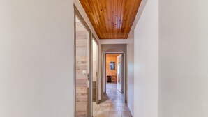 Un couloir avec un plafond en bois et un sol carrelé, qui mène à une pièce dotée d’une porte.