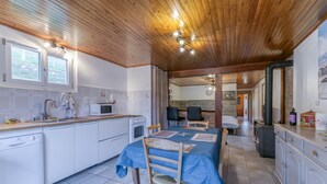 Une cuisine avec un plafond en bois, des armoires blanches, une table à manger avec des chaises et une vue sur un paysage montagneux.